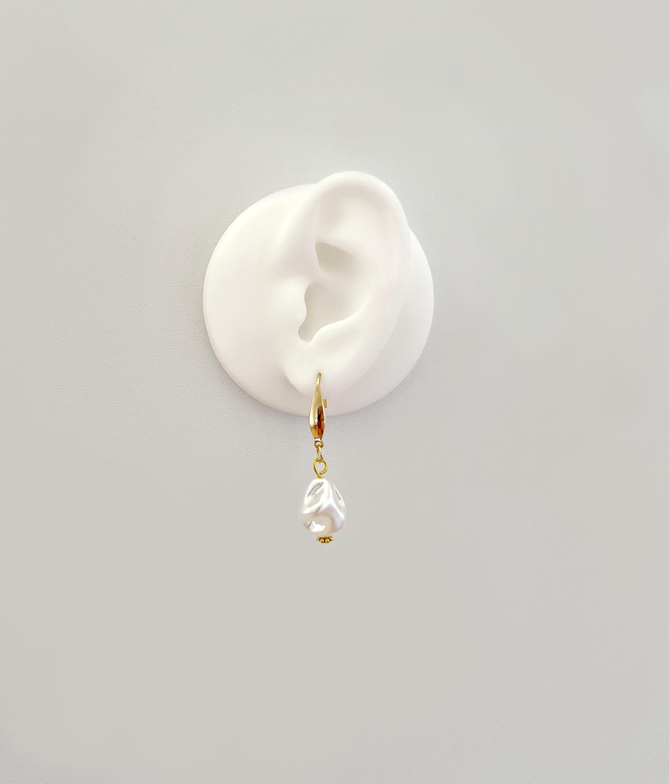 A single gold hoop earring with a dangling clear teardrop-shaped pearl, displayed on a white silicone ear stand against a light gray background.