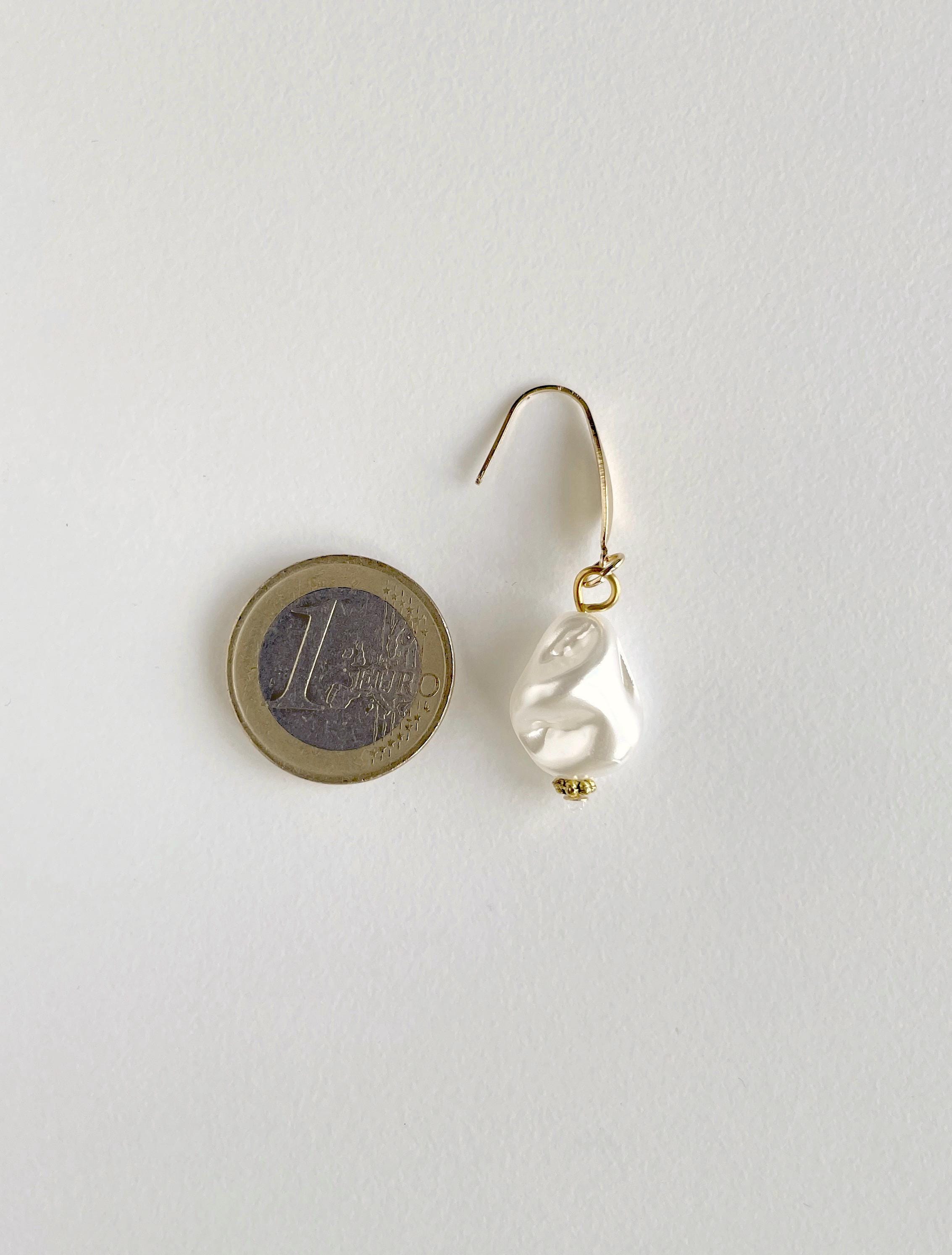 A single gold-tone dangle earring with a white irregular pearl bead, shown next to a 1 Euro coin for scale on a plain white background.