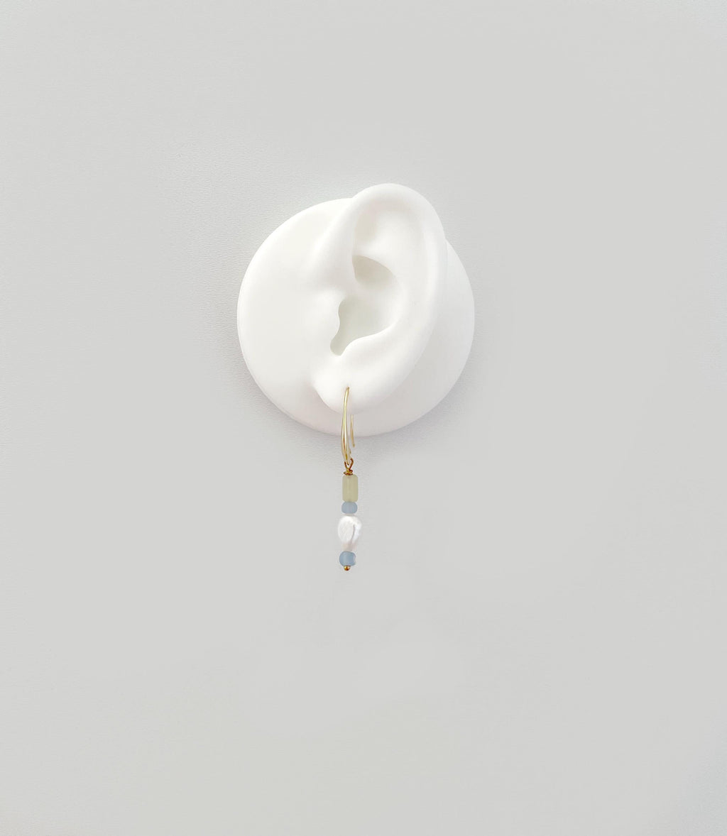 A delicate gold hoop earring with small pale blue and white beads, displayed on a white silicone ear stand against a light gray background.
