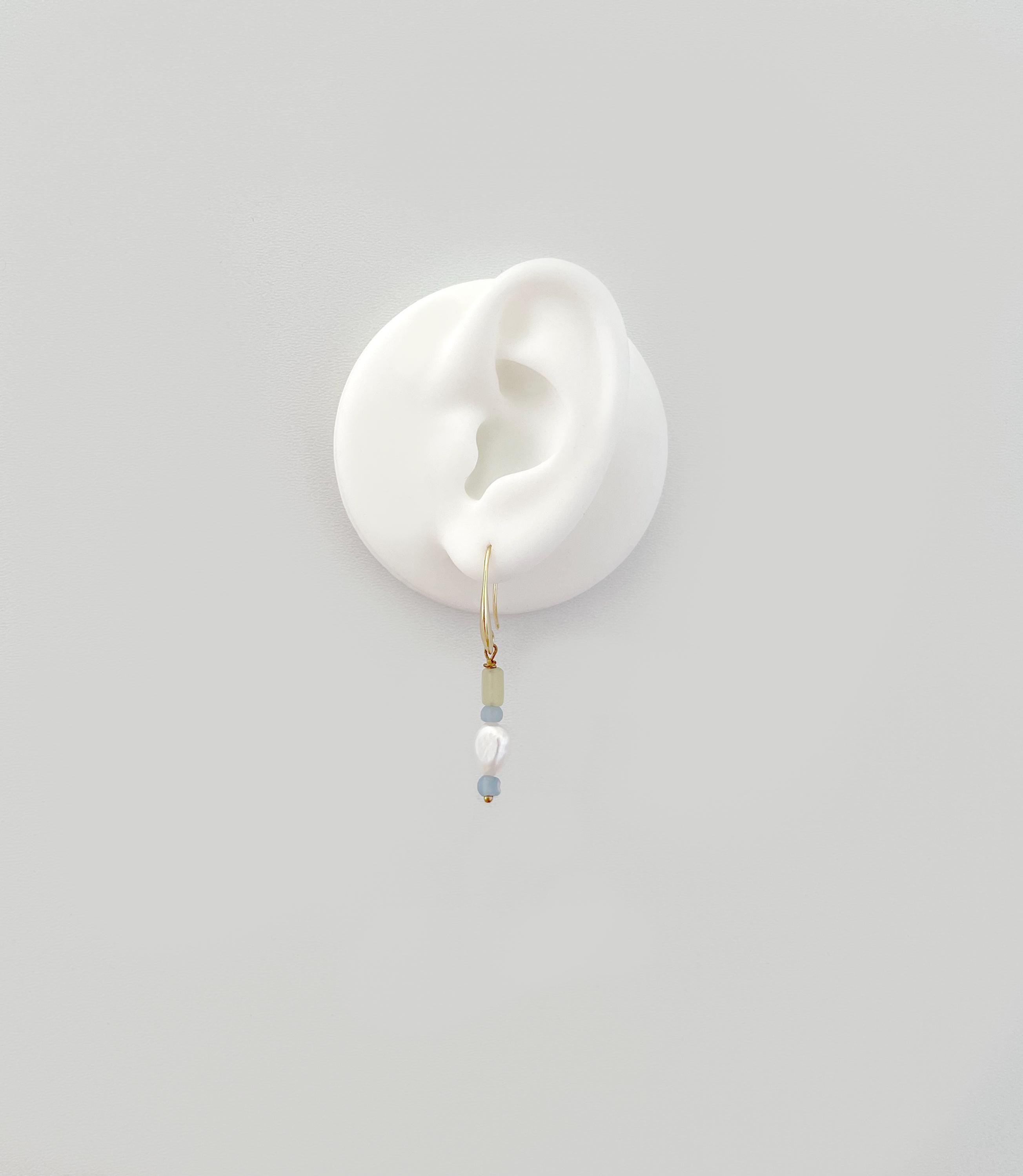 A delicate gold hoop earring with small pale blue and white beads, displayed on a white silicone ear stand against a light gray background.