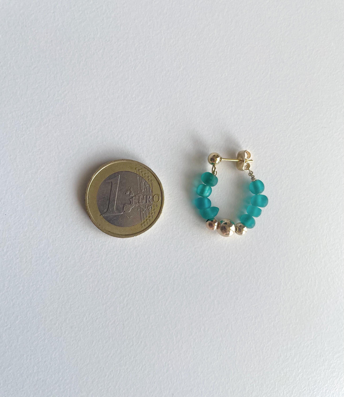 A pair of small hoop earrings with turquoise beads and gold-toned metal beads, shown next to a 1 Euro coin for scale on a plain white background.