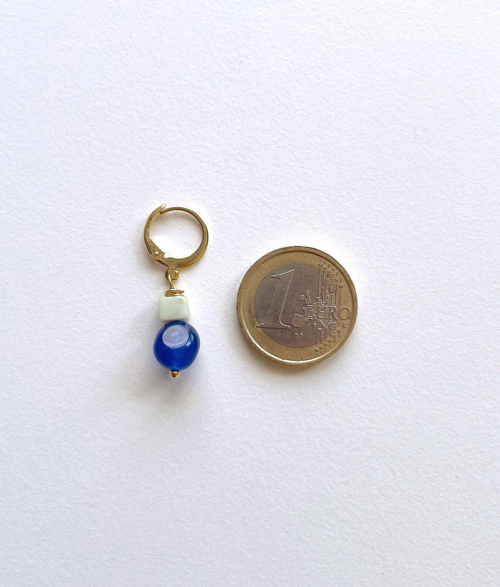 A small gold plated huddle hoop earring with a white bead and a blue natural jade bead, shown next to a 1 Euro coin for scale on a white background.