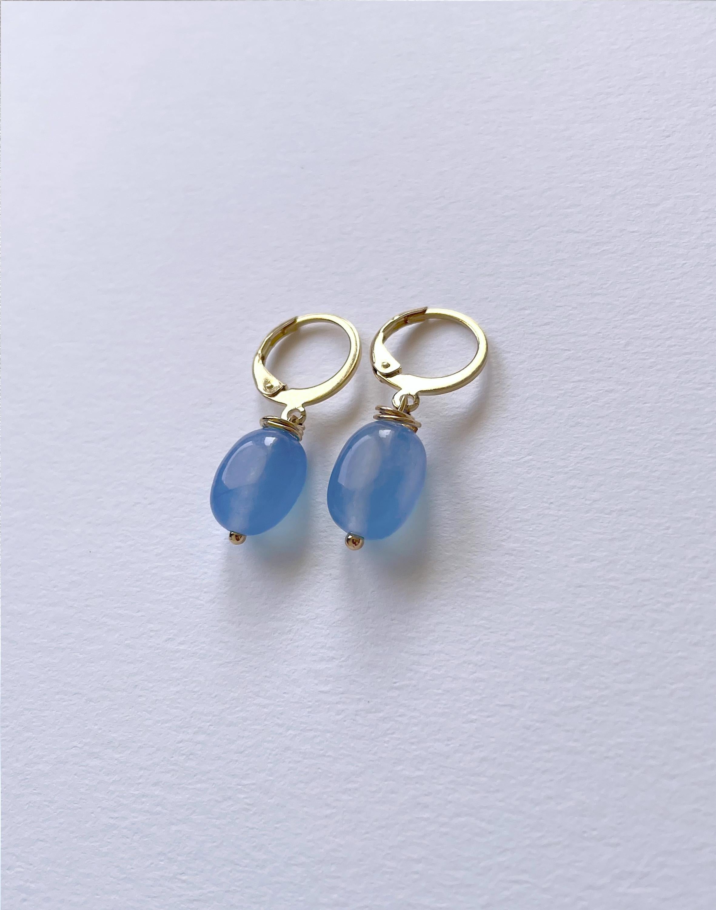 A pair of gold hoop earrings with smooth, oval light blue bead drops, displayed on a clean, light gray textured surface.