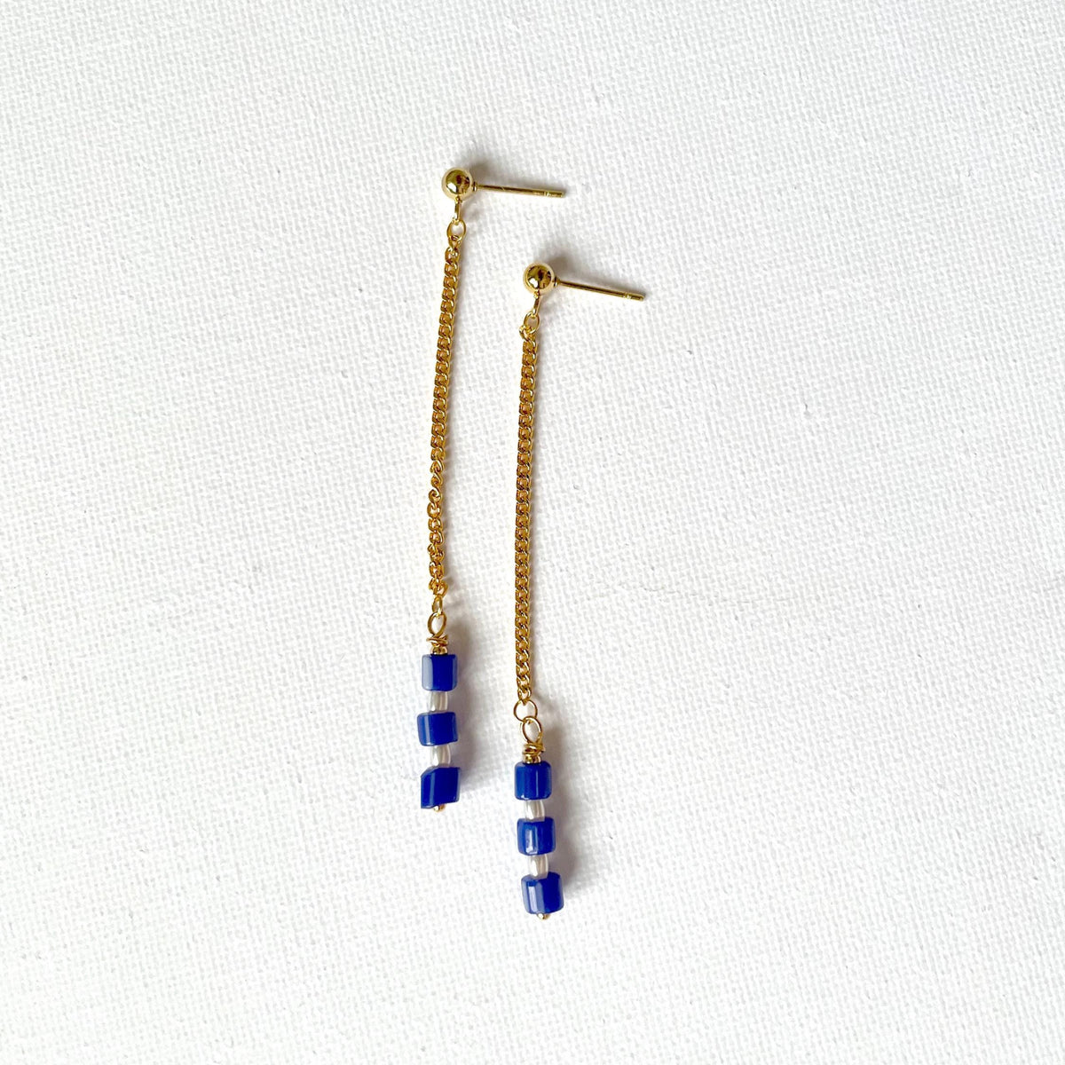 A pair of gold dangle earrings with small blue and white striped beads with natural pearls, displayed on a textured white background.