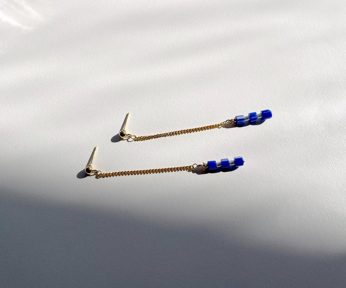 A pair of gold-toned dangle earrings with small blue bead accents with real pearls, displayed on a white surface with soft shadows.