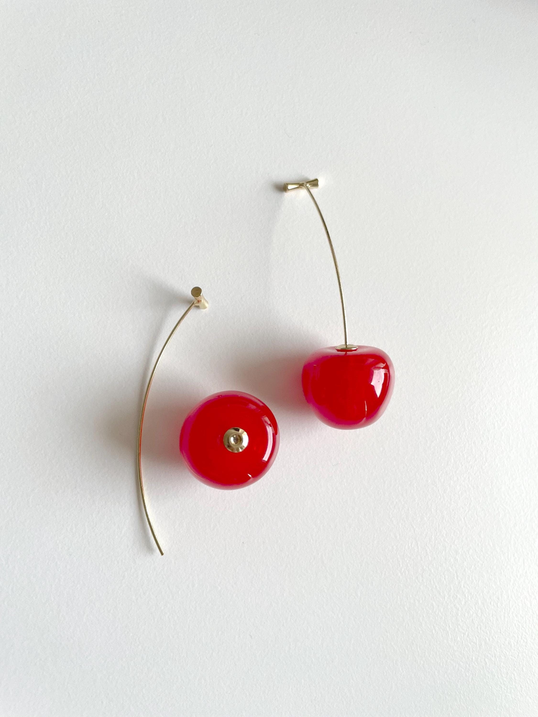 Glossy red cherry-shaped drop earrings with thin gold wire stems, shown against a plain white background.