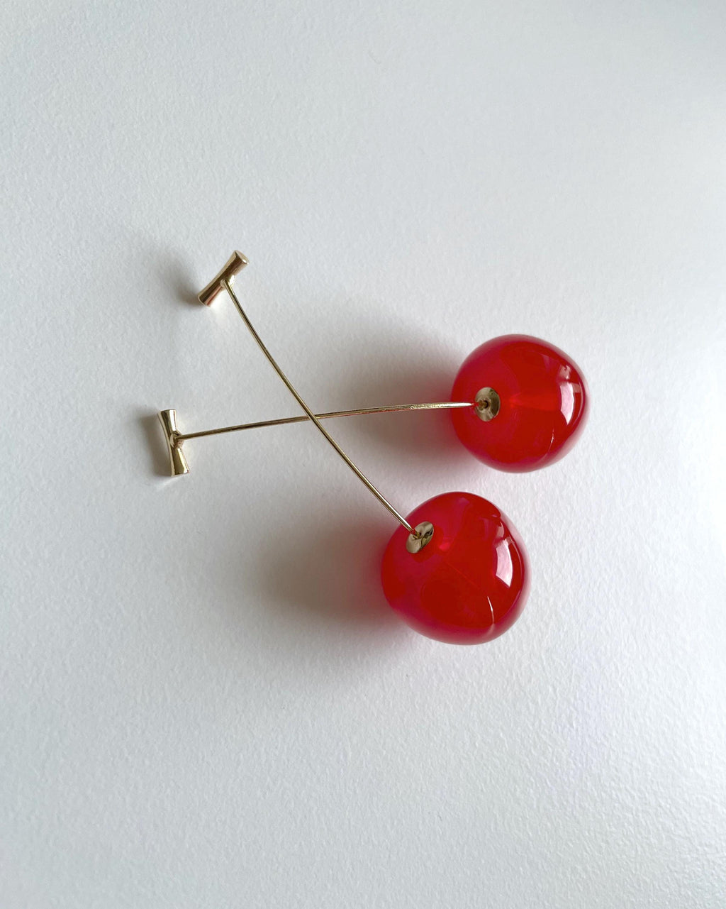 Red cherry drop earrings with gold-tone posts and backing, photographed on a plain white surface.