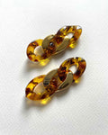 A pair of amber and gold chain-link earrings on a textured white background.