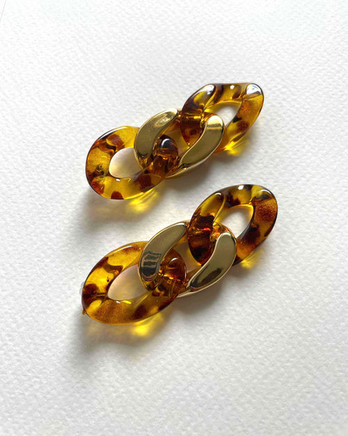 A pair of amber and gold chain-link earrings on a textured white background.