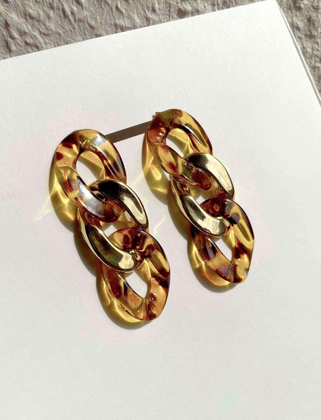 A pair of chunky chain-link drop earrings in a glossy amber and tortoiseshell pattern, displayed on a white card.