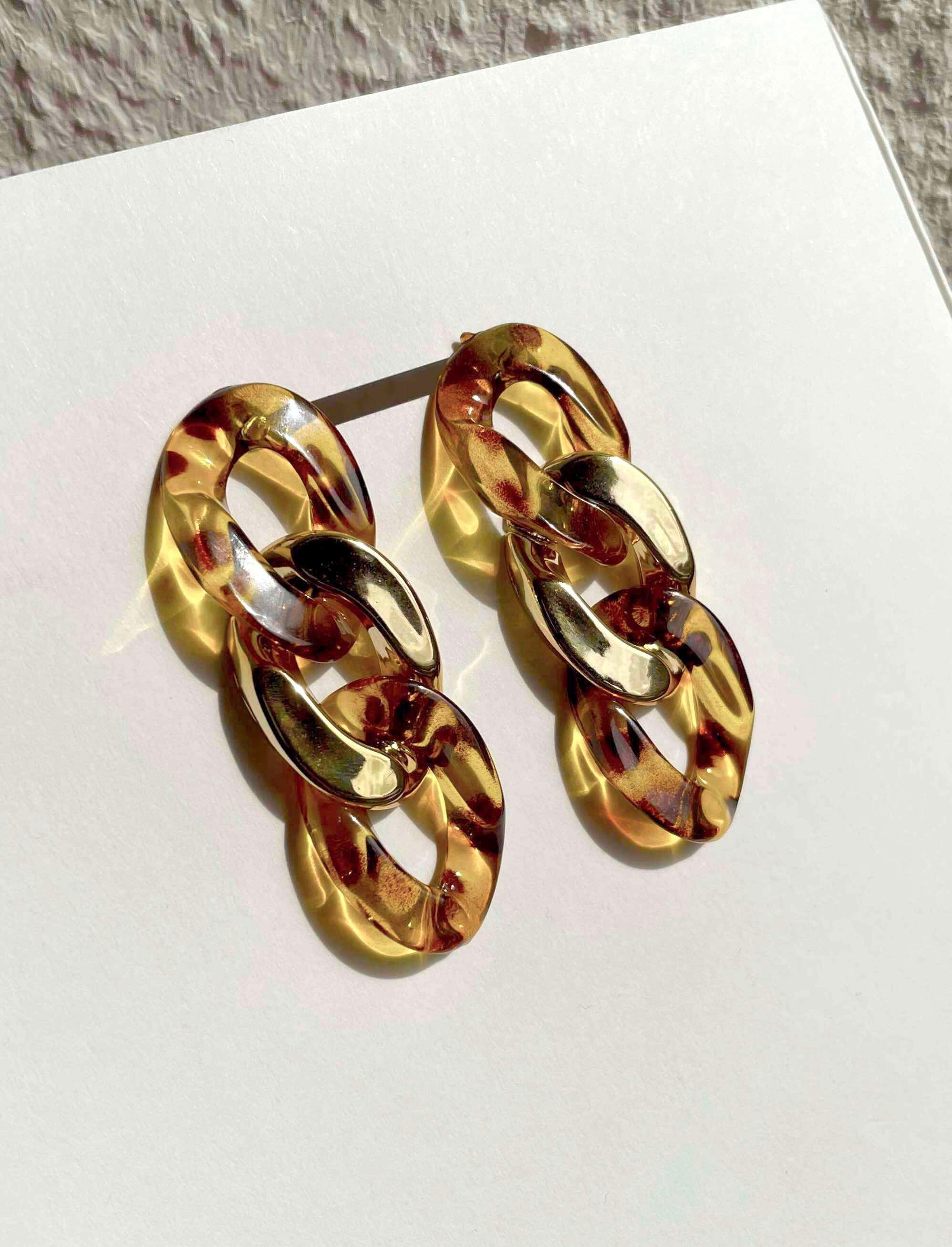 A pair of chunky chain-link drop earrings in a glossy amber and tortoiseshell pattern, displayed on a white card.
