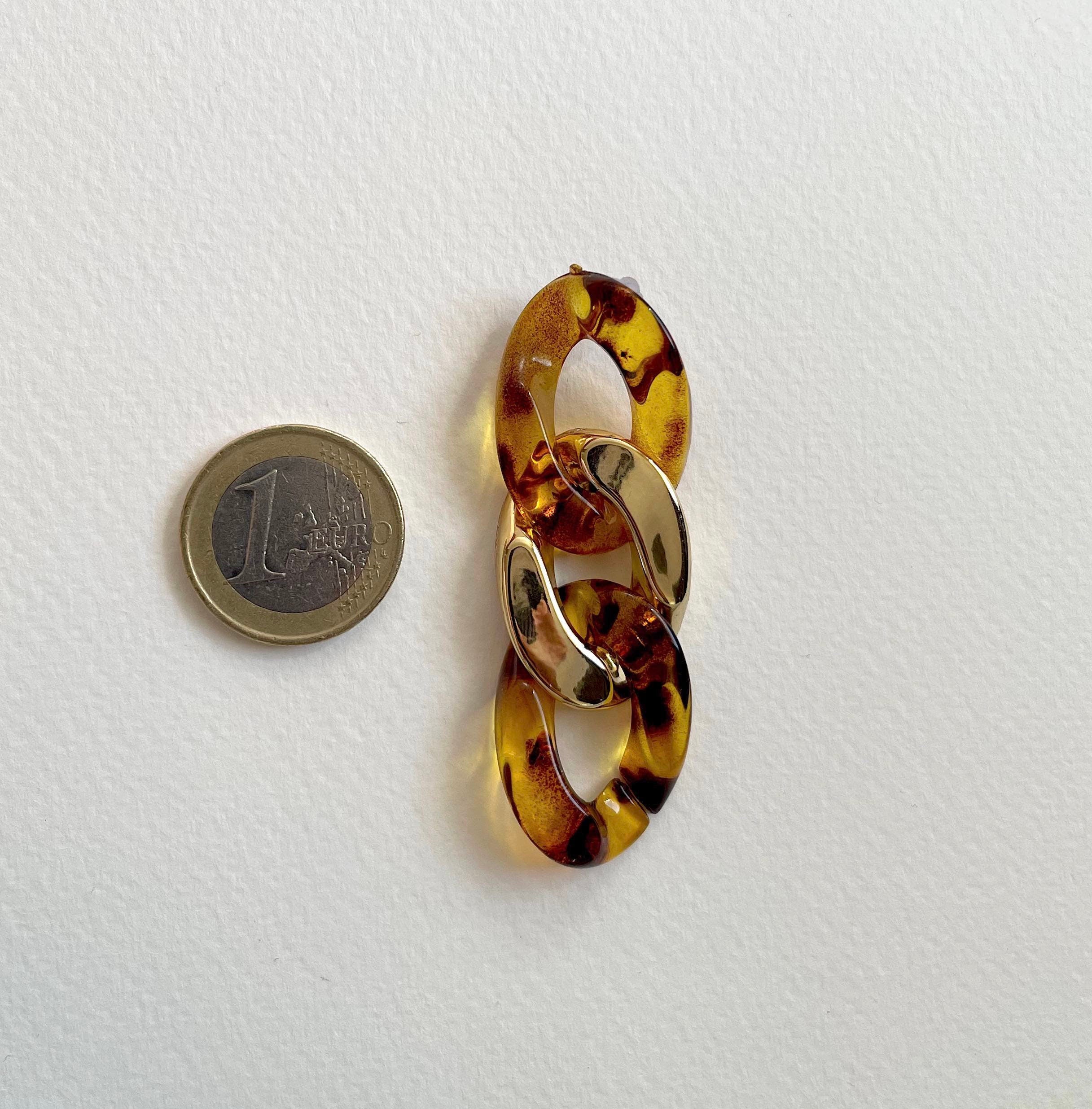 A tortoiseshell link brooch with gold-toned metal accents, shown next to a 1 Euro coin for scale on a white textured background.