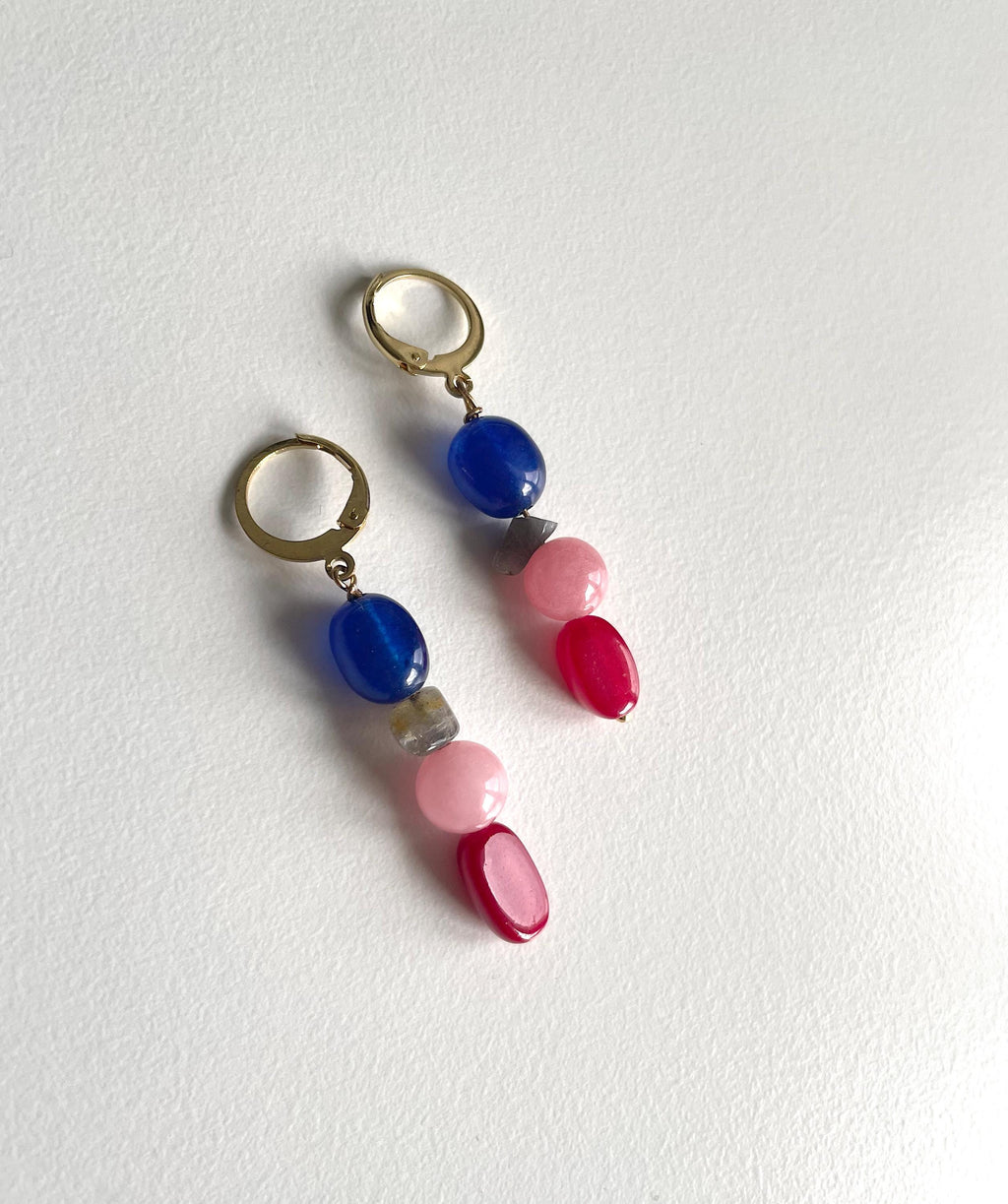 A pair of drop earrings with gold-tone hoops and natural gemstone beads, featuring blue, pink, and red beads on a textured white background.