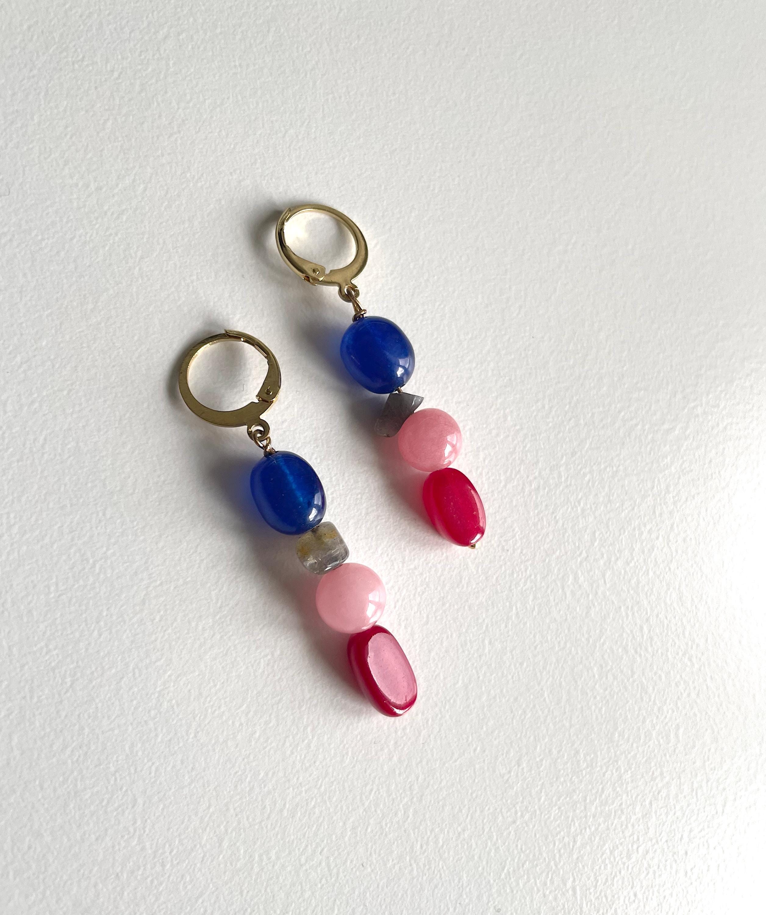 A pair of drop earrings with gold-tone hoops and natural gemstone beads, featuring blue, pink, and red beads on a textured white background.