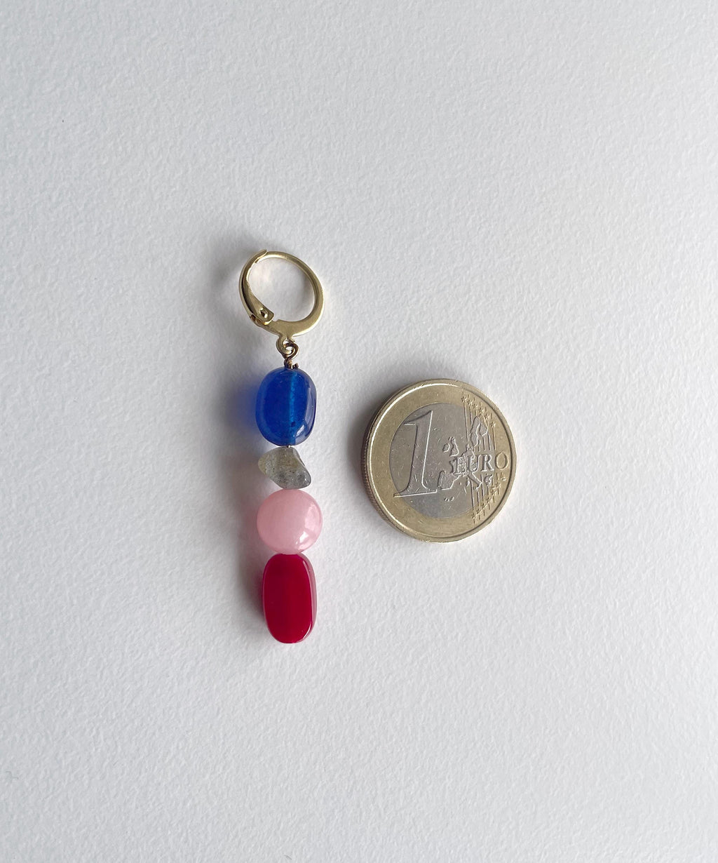A small gold-tone keyring charm with four dangling gemstone beads in blue, clear, pink, and red, shown next to a 1 Euro coin for scale on a white background.