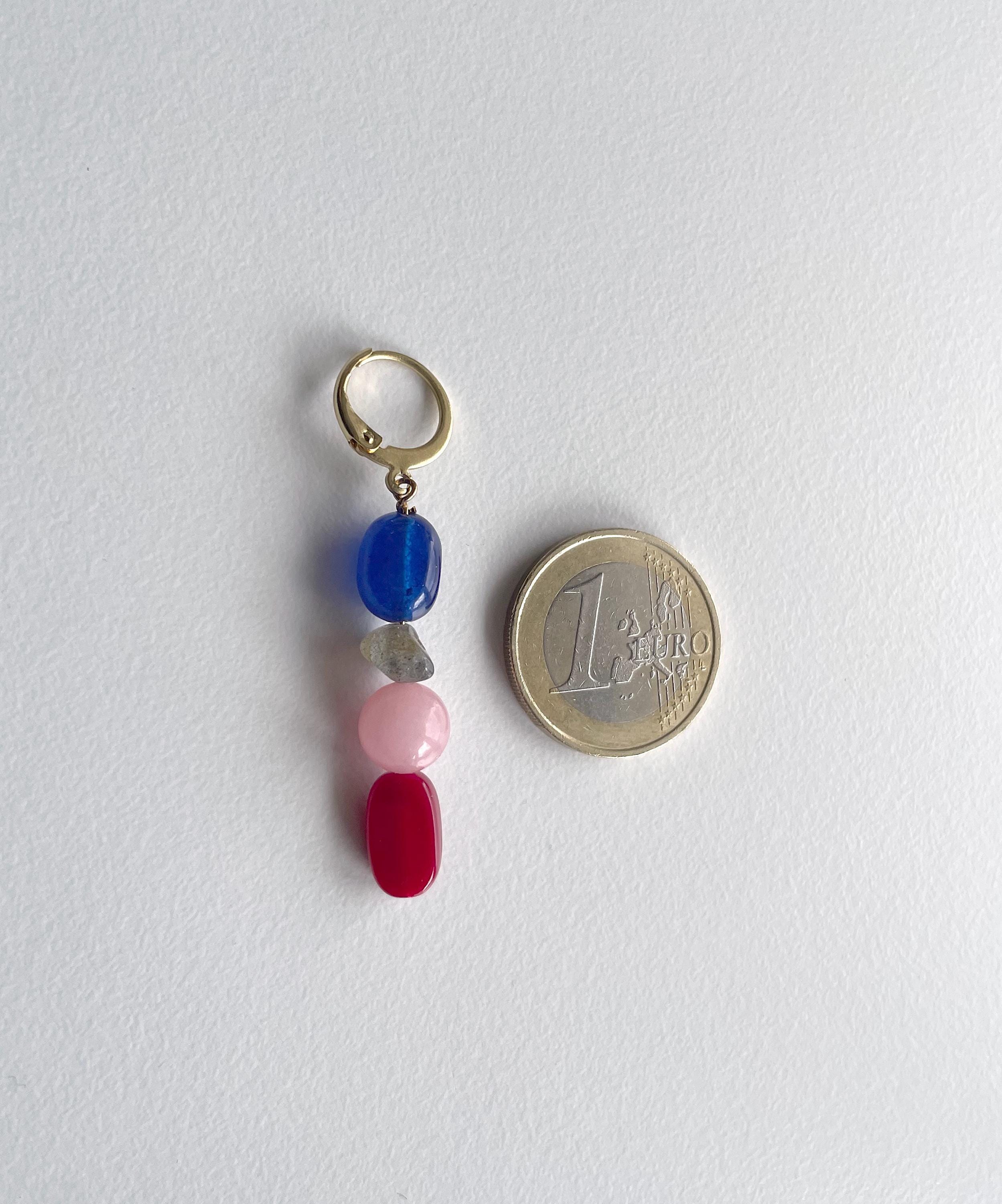 A small gold-tone keyring charm with four dangling gemstone beads in blue, clear, pink, and red, shown next to a 1 Euro coin for scale on a white background.