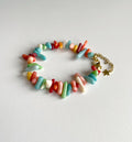 A colorful beaded bracelet made of small cylindrical beads in pastel and bright shades of blue, red, green, pink, yellow, and white, with a gold chain extender and star clasp, photographed on a light gray background.