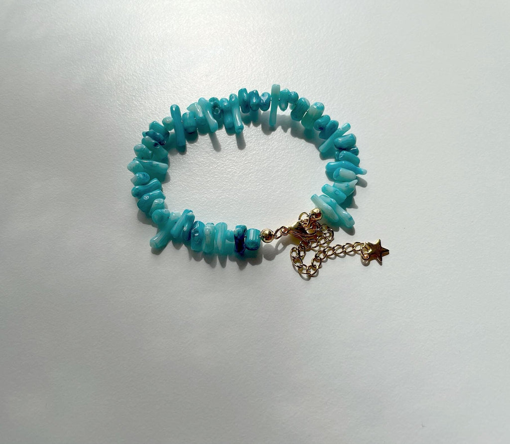 A turquoise coral bracelet with a gold-tone chain extender and star charm, displayed on a light gray surface.