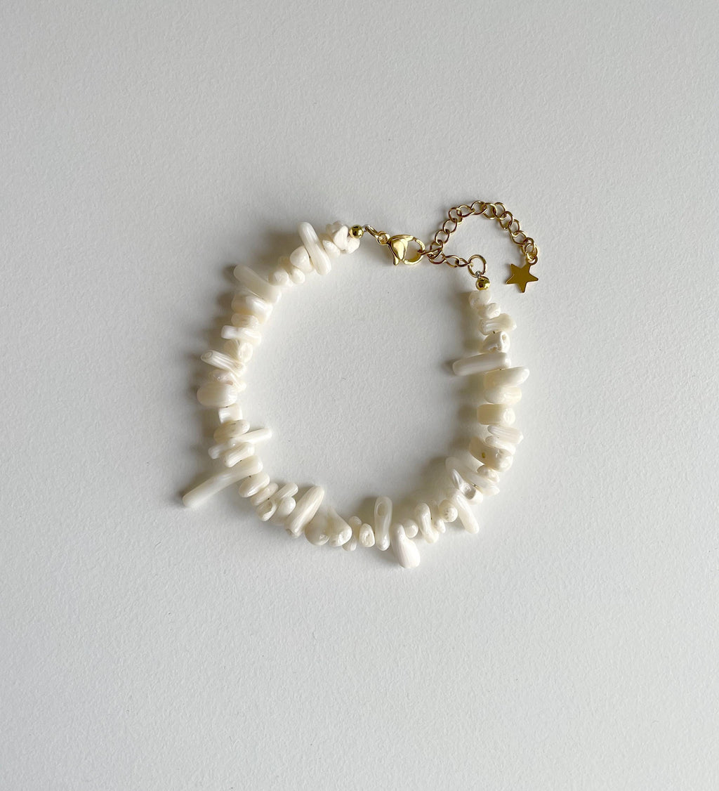 A delicate bracelet featuring irregular white shell-like beads on a gold-tone chain with a star charm, displayed on a light gray background.