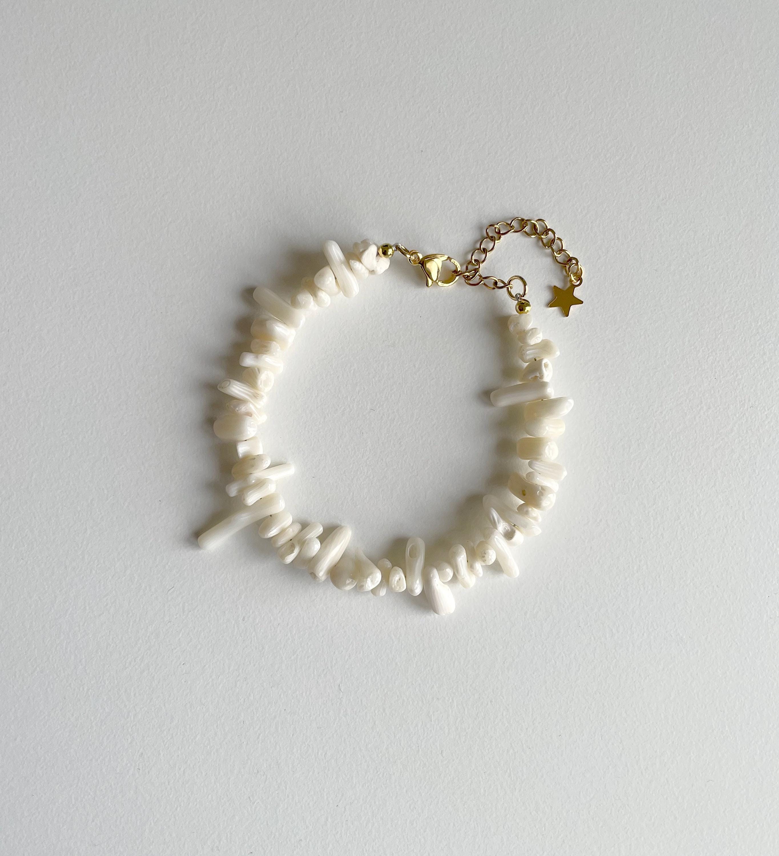 A delicate bracelet featuring irregular white shell-like beads on a gold-tone chain with a star charm, displayed on a light gray background.