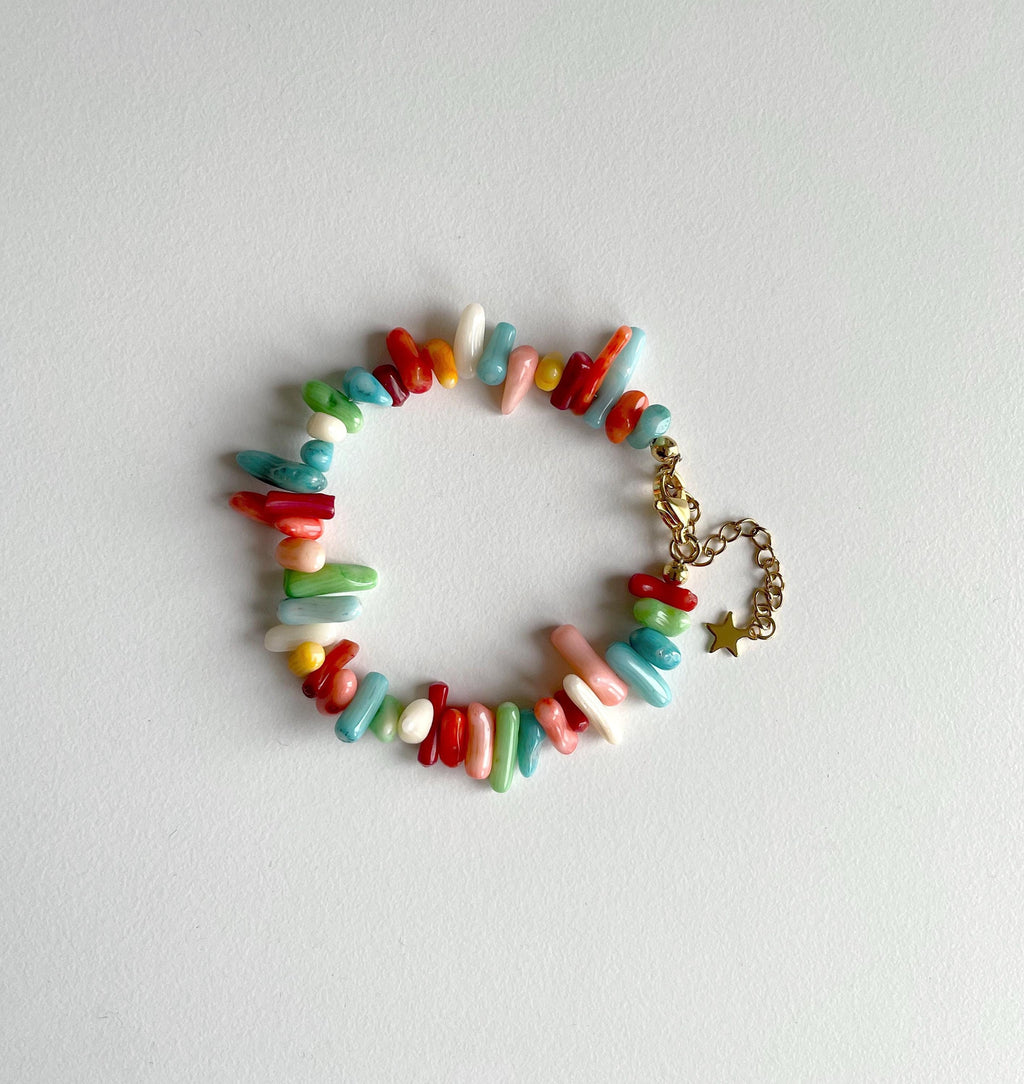 A multicolor beaded bracelet made of small cylindrical and irregular beads in red, blue, green, pink, yellow, and white, with a gold-tone chain and star charm, displayed on a light gray background.