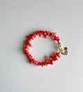 A coral red chip bracelet with a gold star charm and lobster clasp, displayed on a light gray background.