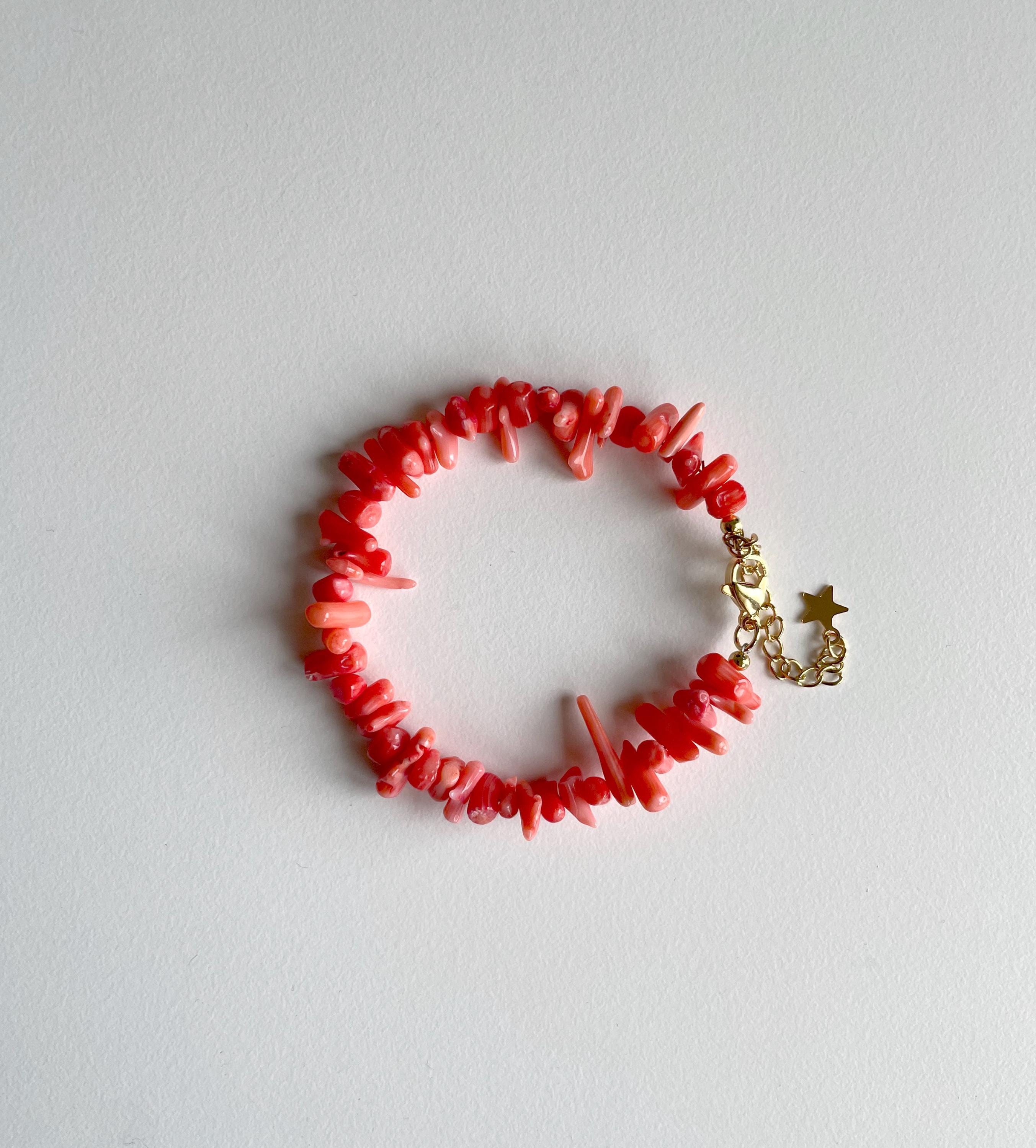 A coral red chip bracelet with a gold star charm and lobster clasp, displayed on a light gray background.