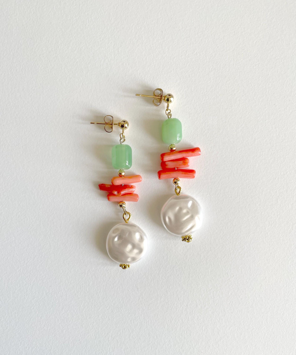A pair of drop earrings featuring a light green stone bead, a cluster of coral-like orange beads, a white baroque pearl, and gold-tone posts, displayed on a clean white background.