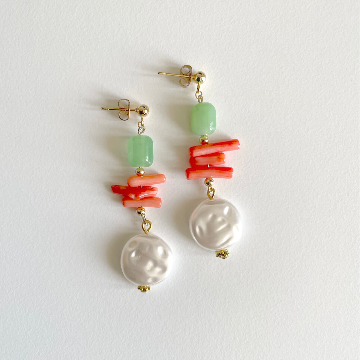 A pair of drop earrings featuring a light green stone bead, a cluster of coral-like orange beads, a white baroque pearl, and gold-tone posts, displayed on a clean white background.