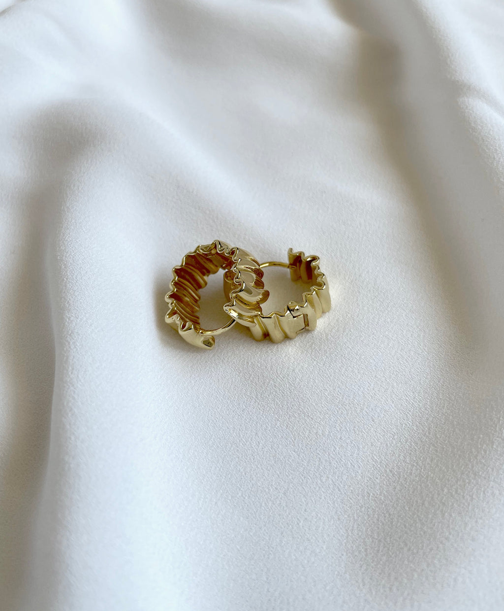 Two gold-toned 18K gold plated textured huggie hoop earrings with a wavy, layered design, displayed on a soft, draped white fabric background.

waterproof earrings

skin friendly earrings

sea water friendly earrings

round hoops

modern hoops

modern gold hoops

hoops

hoop earrings

golden hoops

gold hoops

gold plated hoops

cute hoops

crinkled hoops

contemporary hoops

circular hoops

brass hoops

brass hoop earrings