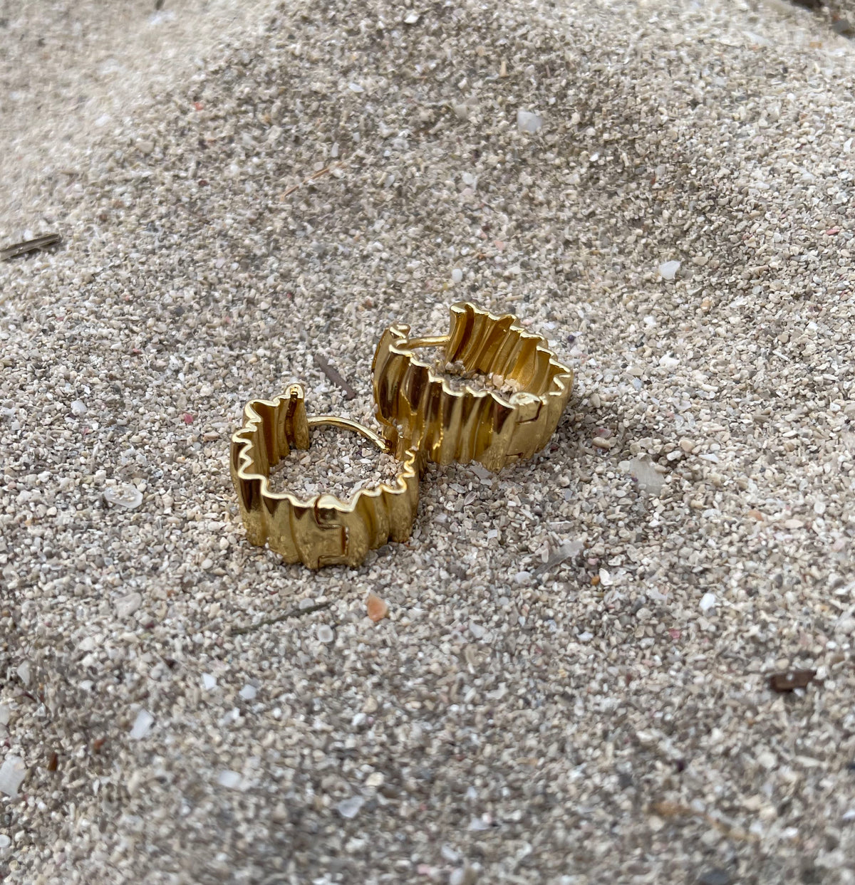 A pair of 18K gold plated gold-toned textured hoop earrings resting on a sandy, gravel-covered surface.

waterproof earrings

skin friendly earrings

sea water friendly earrings

round hoops

modern hoops

modern gold hoops

hoops

hoop earrings

golden hoops

gold hoops

gold plated hoops

cute hoops

crinkled hoops

contemporary hoops

circular hoops

brass hoops

brass hoop earrings