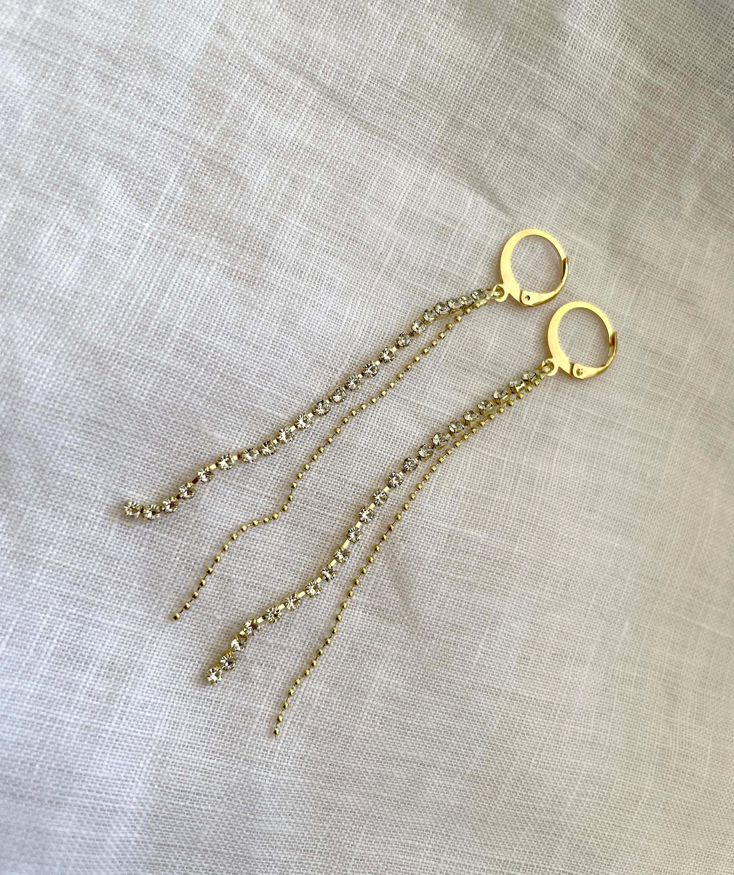A pair of gold hoop dangle earrings with delicate chain drops, displayed on a textured beige linen fabric background.