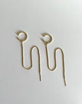 A pair of gold plated cuff chain earrings with textured circular cuffs and long wavy drop chains ending in pointed tips, displayed on a plain light gray surface.