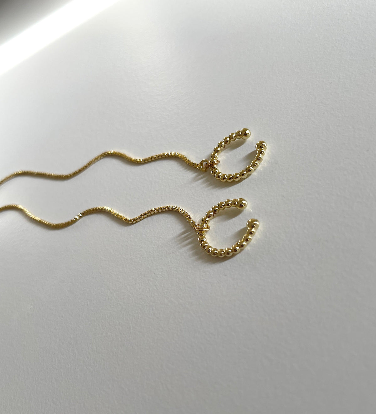 A pair of gold wavy cuff chain earrings with textured beaded ends, displayed on a clean white surface.