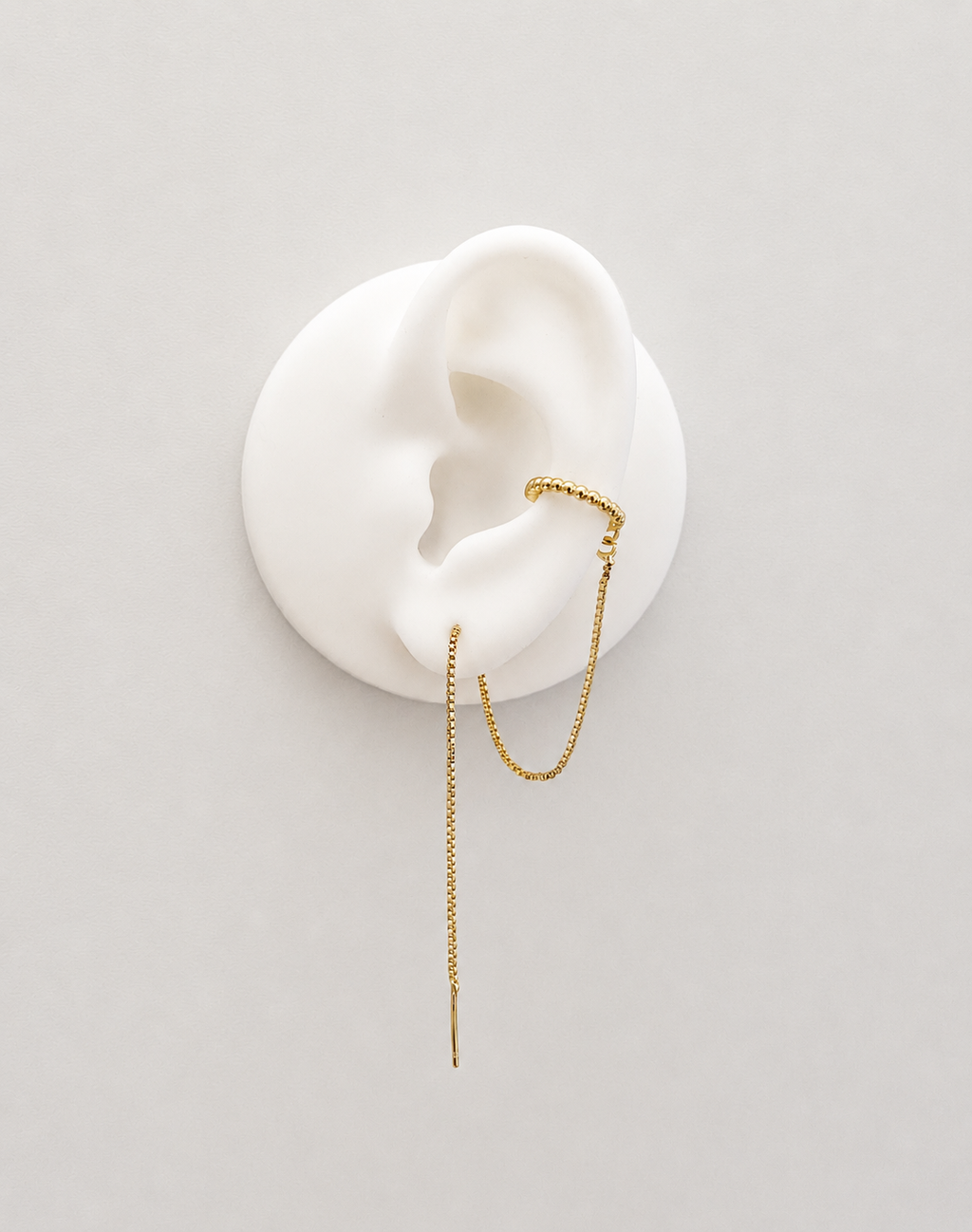 A delicate gold plated threader earring with a small curved cuff and a long dangling chain, displayed on a white ear-shaped mannequin against a light gray background.