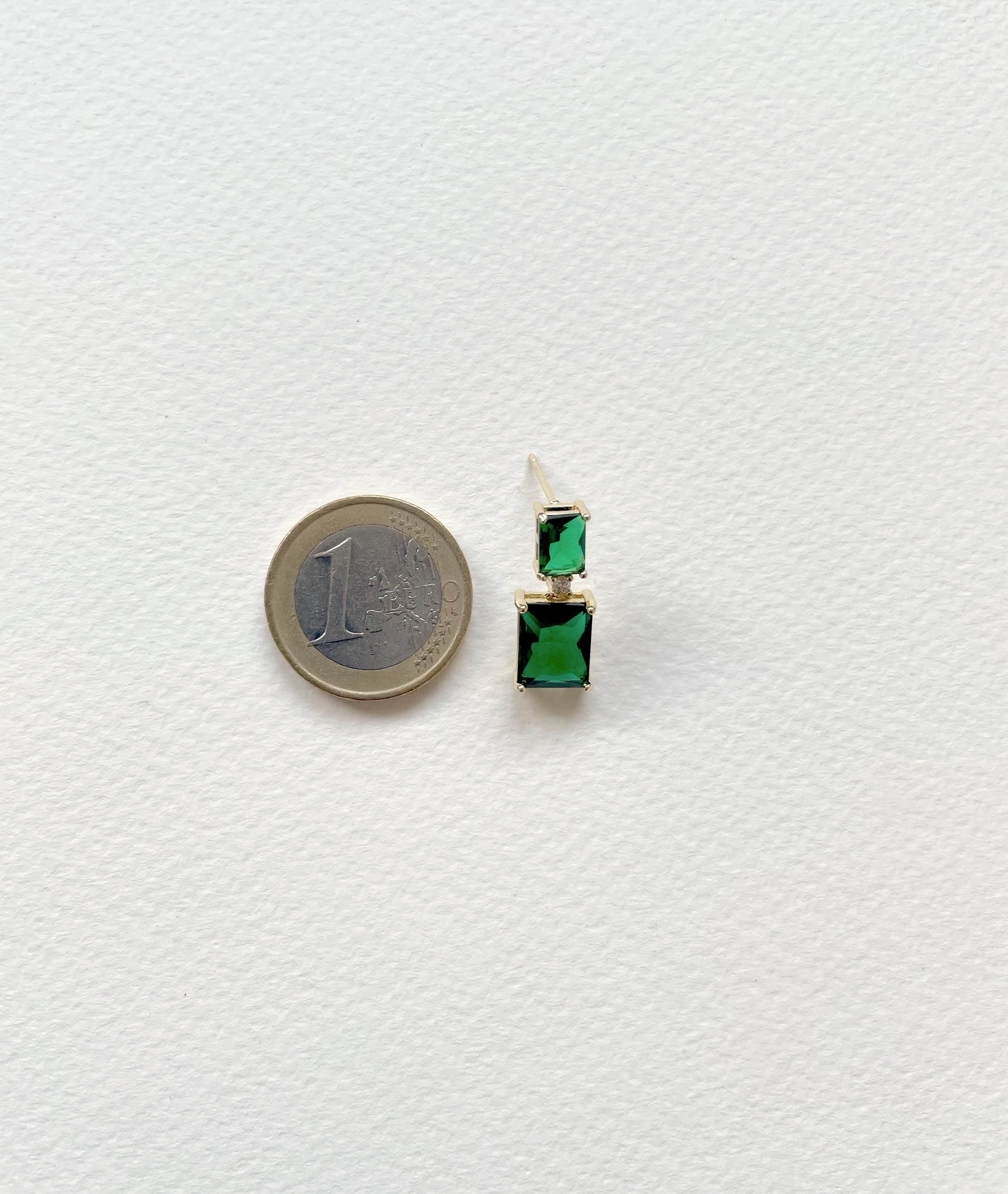 A single drop earring with a gold-toned post and two stacked rectangular green gemstones, shown next to a 1 Euro coin for scale on a textured white background.
