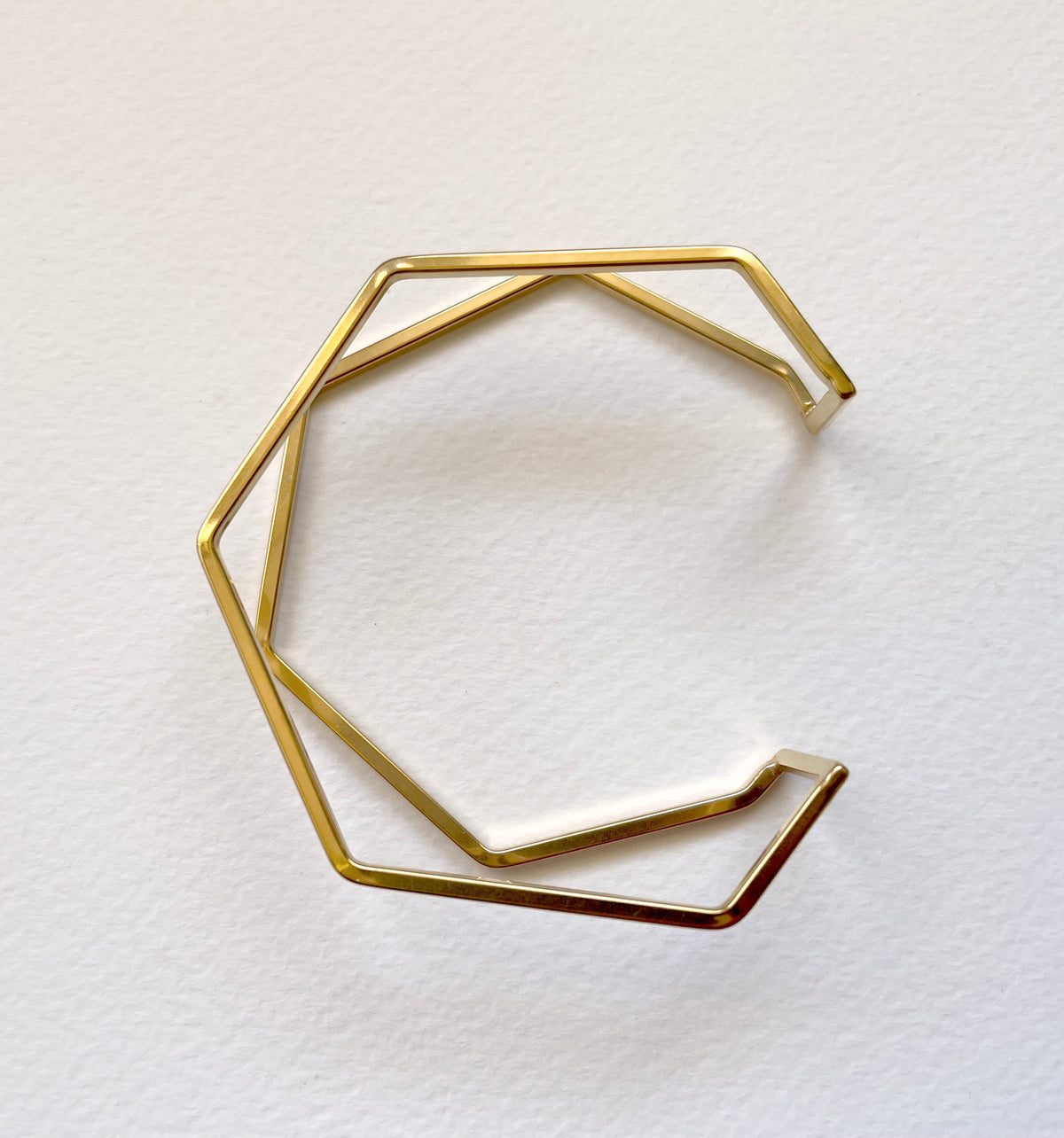 A geometric open cuff bracelet made of thin gold-toned metal bars, photographed on a plain white textured background.