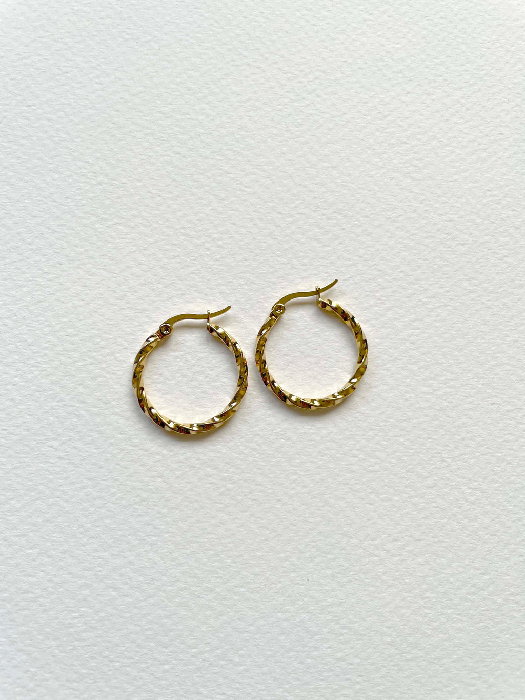 A pair of small gold hoop earrings with a textured, woven-like finish, displayed on a clean white textured background.