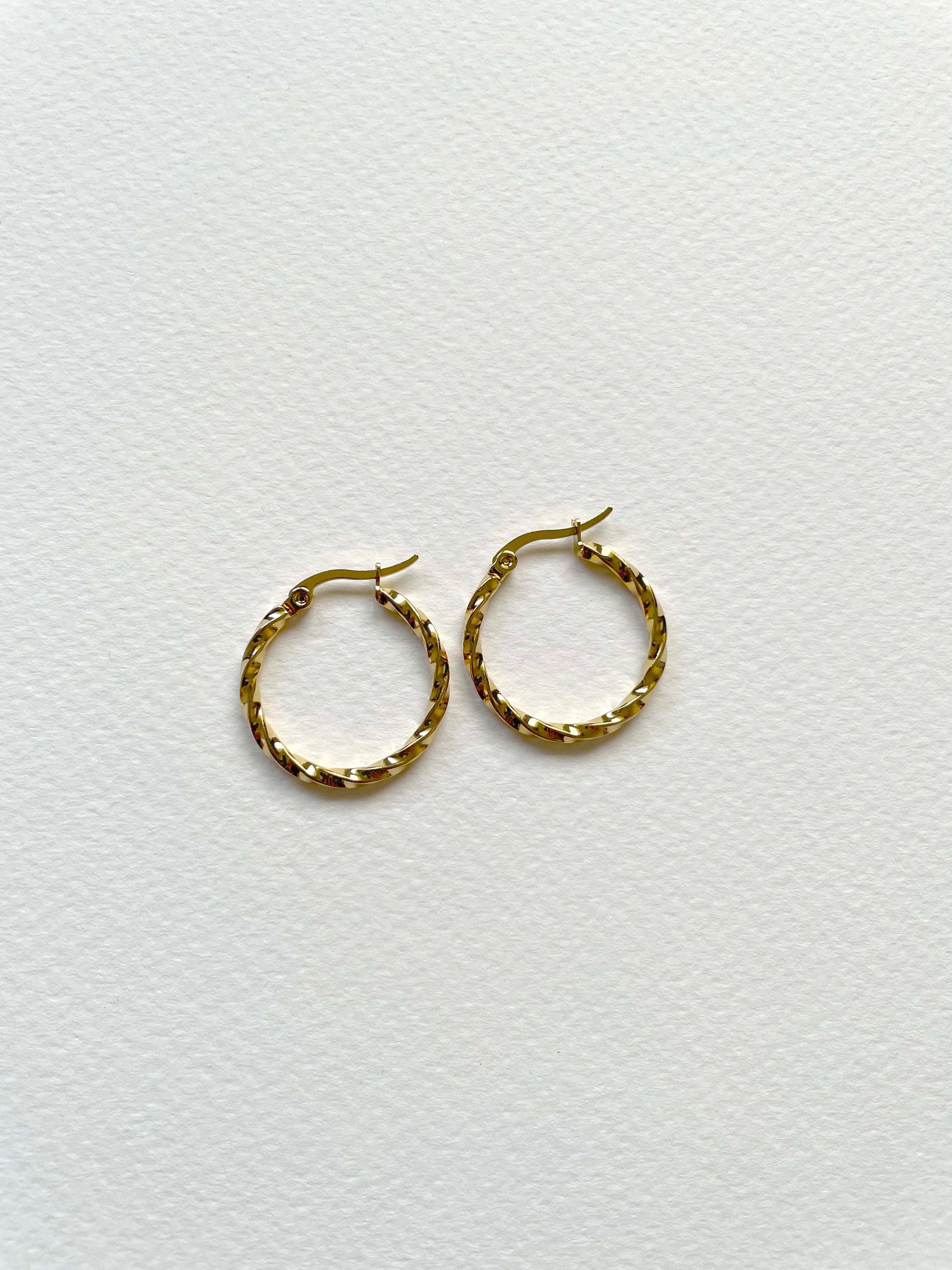 A pair of small gold hoop earrings with a textured, woven-like finish, displayed on a clean white textured background.