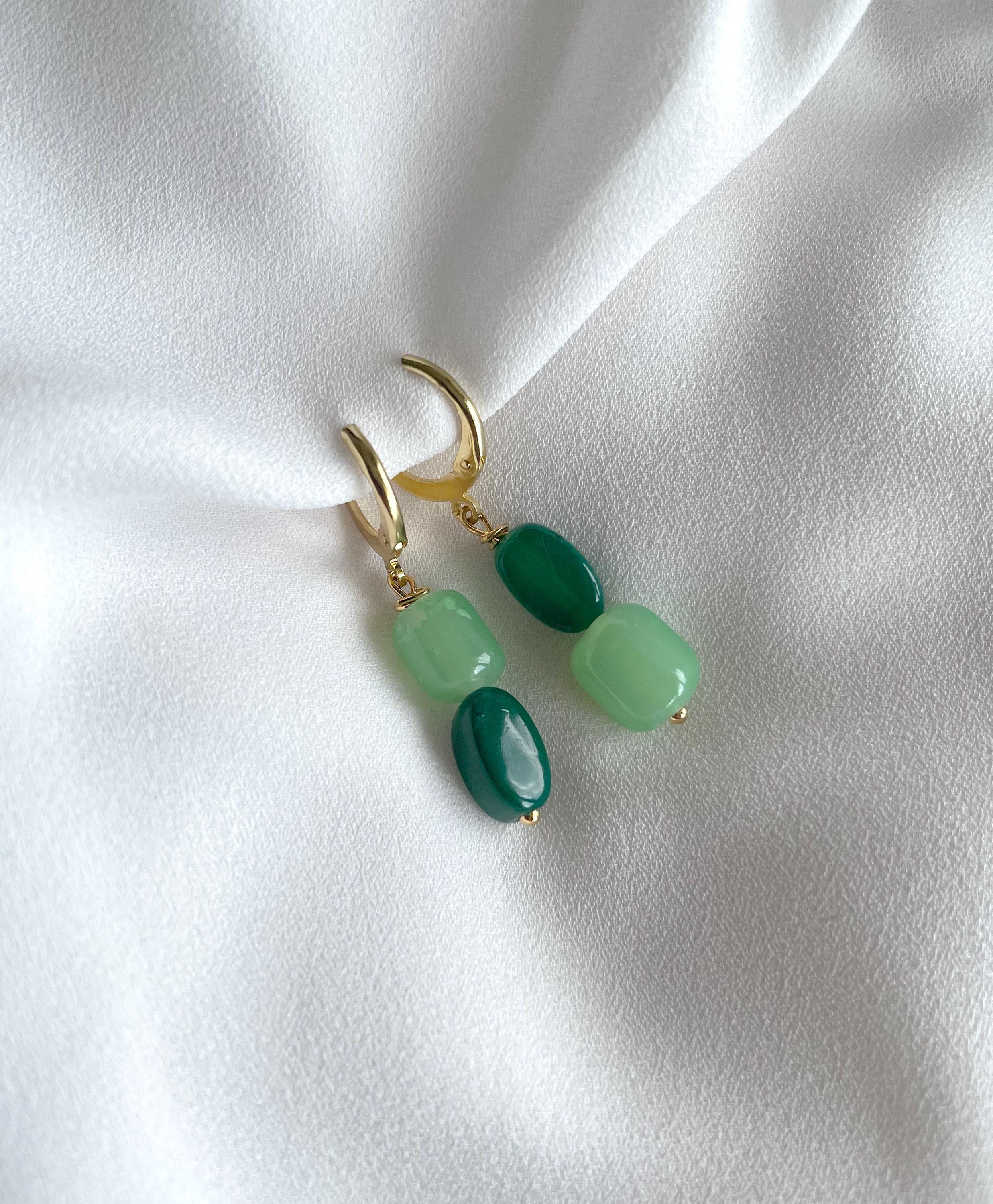 A pair of gold hoop earrings with green beads, displayed on a draped white fabric background.