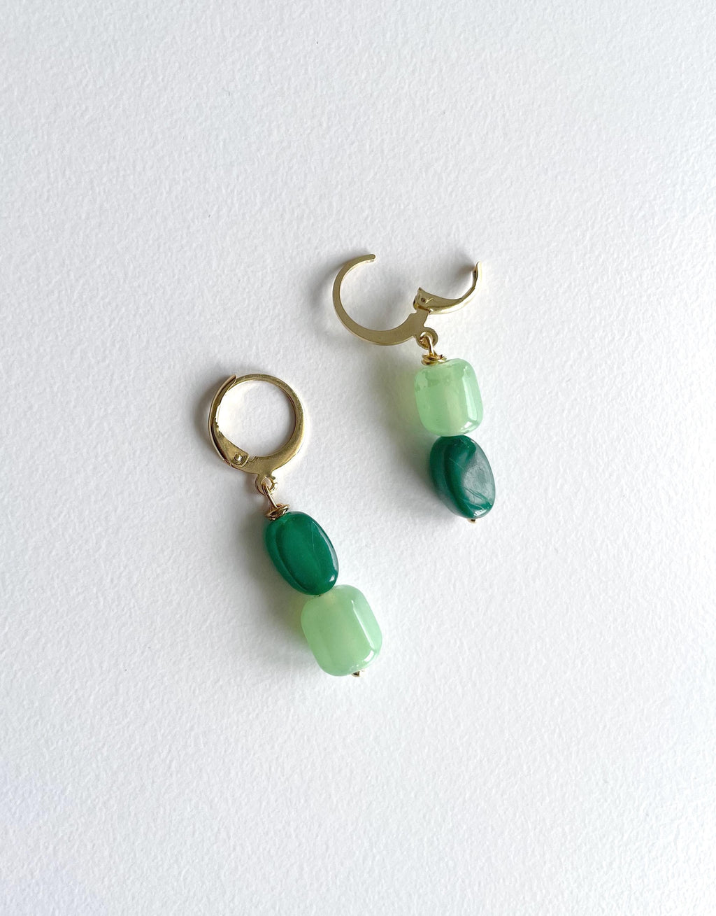 A pair of gold hoop earrings with green stone beads, displayed on a textured white background.