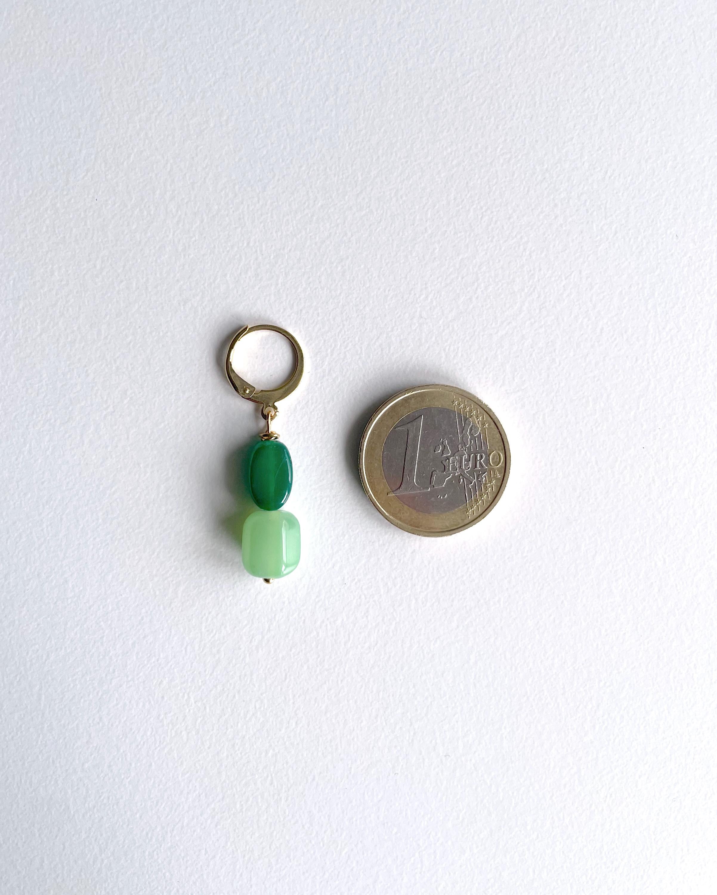 A small jewelry charm or keyring with two green beads and a gold-tone ring, shown next to a 1 euro coin for scale on a white background.
