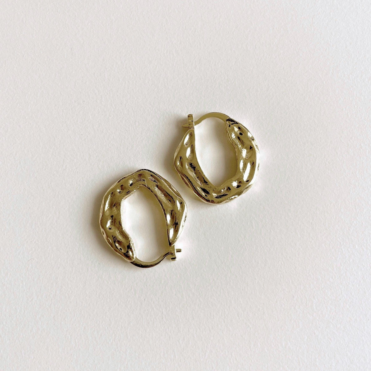 A pair of textured gold plated brass huggie hoop earrings on a clean, off-white background.
