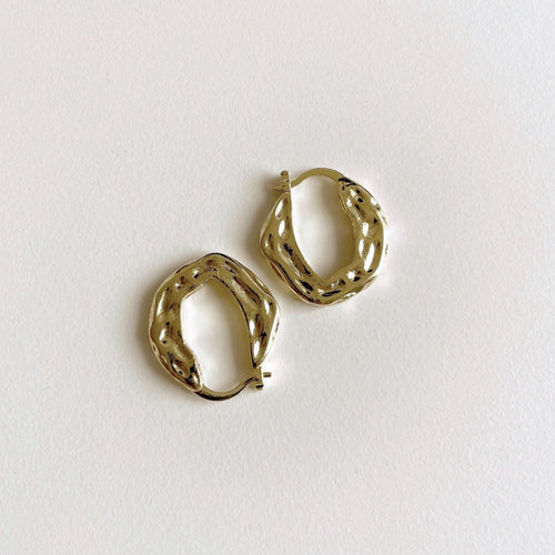 A pair of textured gold plated brass huggie hoop earrings on a clean, off-white background.