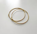 A pair of thin gold hoop earrings with small decorative charms at the closures, displayed on a light gray surface.
