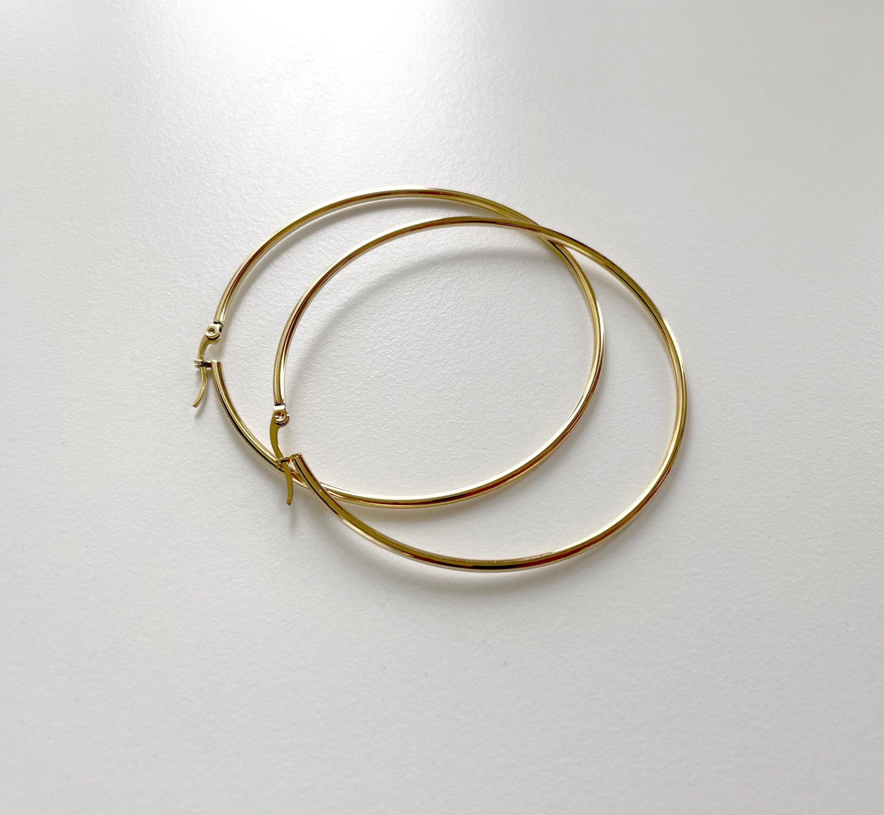 A pair of thin gold hoop earrings with small decorative charms at the closures, displayed on a light gray surface.