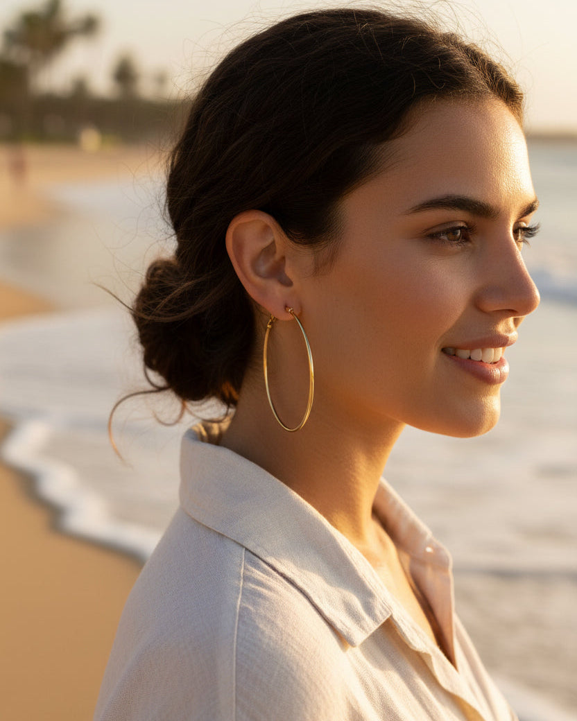 A pair of thin gold hoop earrings with a simple hinge clasp, displayed on a clean, light off-white background.