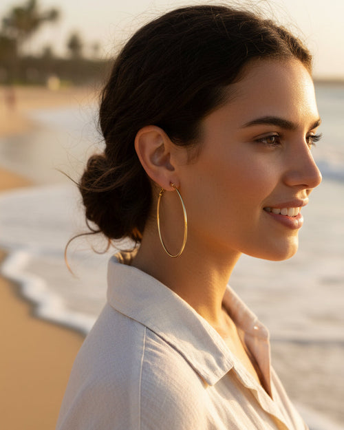 A pair of thin gold hoop earrings with a simple hinge clasp, displayed on a clean, light off-white background.