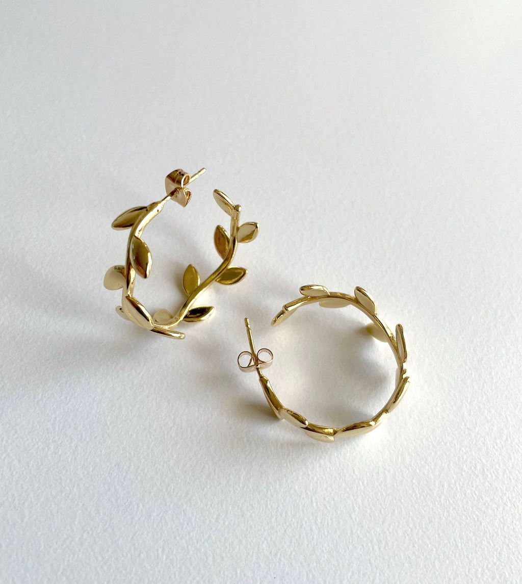 Gold leaf hoop earrings with a textured, organic branch design, displayed on a clean white background.
