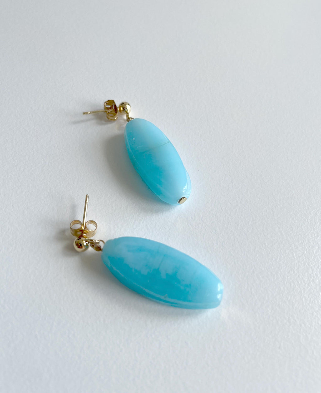 A pair of drop earrings with oval-shaped light blue turquoise beads and gold-colored posts, displayed on a clean white background.